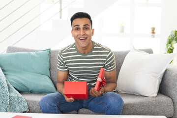 Middle Eastern man sitting on a sofa at home during a video call, holding a gift