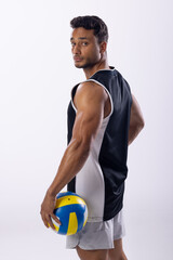 Young biracial man poses confidently in sportswear, holding a volleyball on a white background