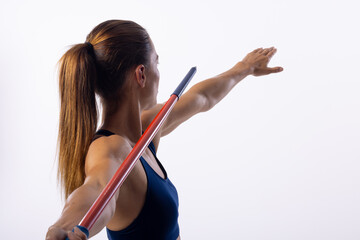 Young Caucasian female athlete practices javelin throwing technique indoors on a white background