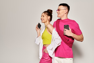 A stylish young couple in love standing closely together in a studio, set against a soft grey background.