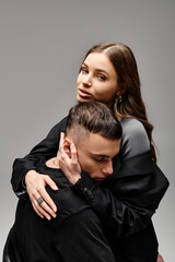 A young couple wrapped in a warm hug, expressing love and closeness in a studio with a grey background.