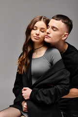 A man and a woman sit closely next to each other, eyes filled with love and serenity, against a grey studio backdrop.