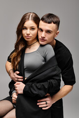 A young man and woman strike a pose together in a studio with a grey background, exuding love and style.