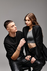 A man and woman sit closely on a chair, expressing love and togetherness in a studio with a grey background.