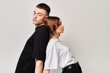 A young couple in love, standing side by side in a studio with a grey background, exuding connection and unity.