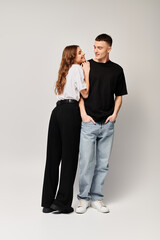 A young couple in love standing next to each other in a studio with a grey background, radiating a sense of togetherness.