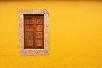 one window with wooden shutters and stone frame. Yellow wall. Stone building, old architecture village in spain. 