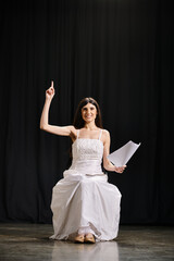 Fototapeta premium Elegant woman in white dress sits gracefully on stage during rehearsals.