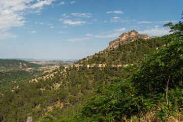 imagen de un paisaje con una montaña llena de árboles verdes, el cielo azul y algunas nubes 