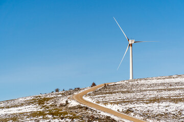 Wind turbine on a snow-covered hill under clear blue sky
