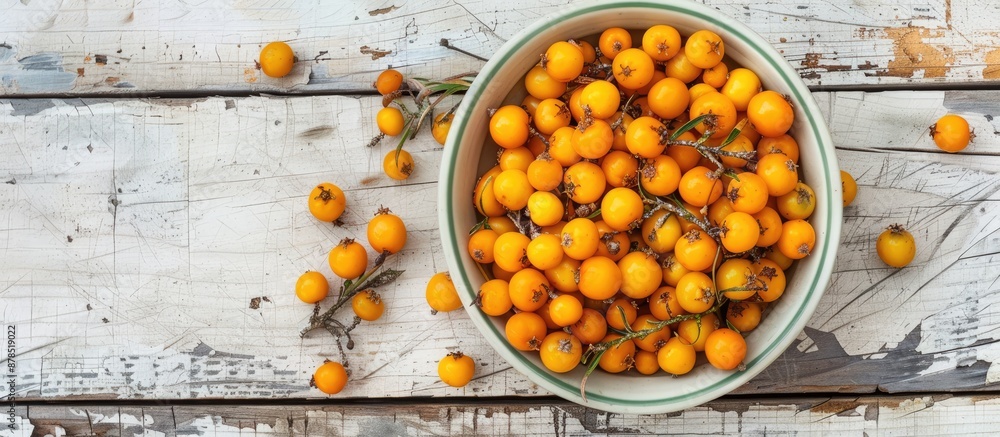 Aufkleber top view of a bowl filled with ripe sea buckthorn berries on a white wooden backdrop, ideal for addi