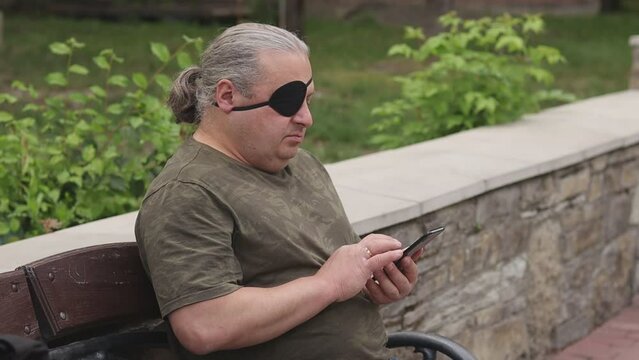 Visually impaired blind man with a black medical patch on his eye looks through the news feed on his phone