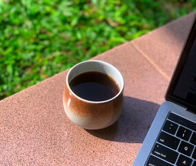 cup of coffee in the morning with blur grass background and laptop keyboard