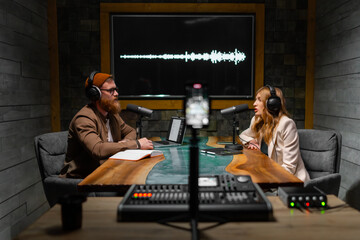 Two radio hosts talking and smiling while sitting near microphones in broadcasting studio