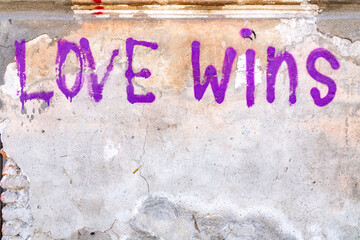 Old concrete wall fragment background with spray writing Love Wins