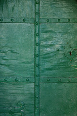 An old green metal door with forged elements for reinforcement as well as a lock, close-up.