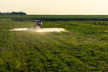 Fototapeta premium A tractor spraying a field with fertilizer, surrounded by trees and land