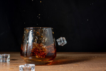 Ice cubes are dropping into a whiskey glass on a wooden table