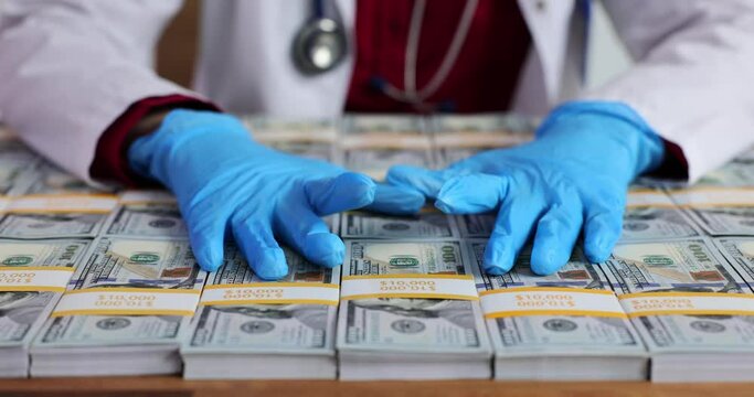 Woman in medical gown places gloved hands on stack of dollar bills