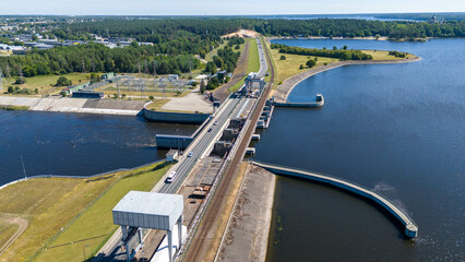 Obraz premium Drone photography of a hydro dam, forest and road with traffic driving over dam during summer day
