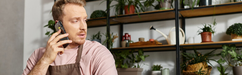 A man in a plant shop sits at a table, engrossed in a phone conversation, showcasing dedication to...