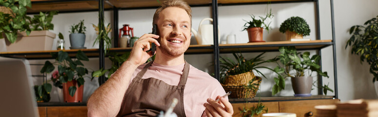 A focused man sits at a desk in a plant shop, engaging in a phone call while managing his small...