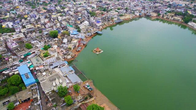 Aerial drone shot backing pan up reveal from shiv brahma temple on lake with crowded buildings to aravalli hills covered by fog showing holy city of Pushar Rajasthan