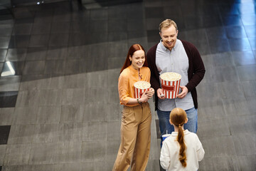 Obraz premium A happy family at the cinema, holding a bucket of popcorn and enjoying a movie together.