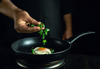 Chef adds chopped green onion to the pan with eggs by hand. Concept of cooking healthy food with egg in hotel kitchen.