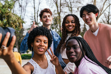 Diverse friends taking a fun selfie outdoors in a park with lush greenery.
