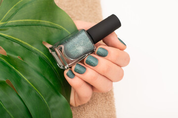 Green Glitter Nail Polish on Female Hand and leaf on background. Close-up of a hand with green glitter nail polish against a green leaf background.