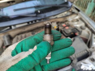 Mechanic holds a car spark plug with oil deposits in his gloved hand