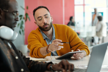 Caucasian and Black colleagues working together on project in modern office using laptop and tablet...