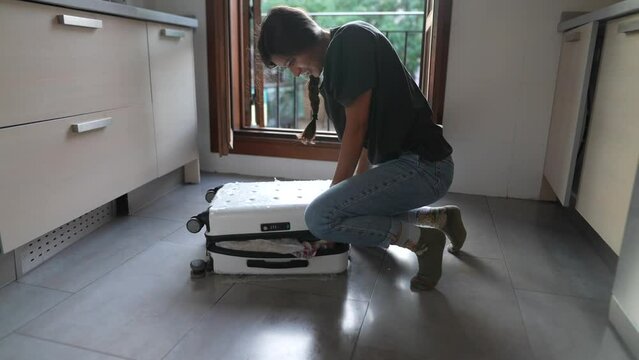 An individual is making an effort to close a heavy packed suitcase in the kitchen