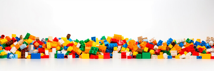 Fototapeta premium White background, white space in the center of picture. A pile of colorful Lego blocks scattered all over the place. The lego bricks of different shapes and sizes to show diversity