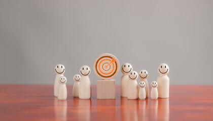 Goal and target concept, wooden figures smiley face around dart board and arrows on table for...