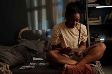 Sad African American woman looking at picture of her sweetheart or died relative while sitting on bed at night during insomnia