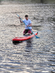 A young man of white race on a SAP swims to the shore in the evening