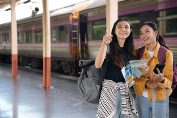 Obraz premium Two young women excitedly planning their next adventure in a bustling train station. Engrossed in a map and smartphone. Exuding wanderlust with luggage by their side