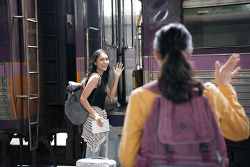 Young woman joyfully waves goodbye to her friend at the train station, capturing the spirit of friendship and adventure. Ideal for portraying the pleasures of a summer getaway