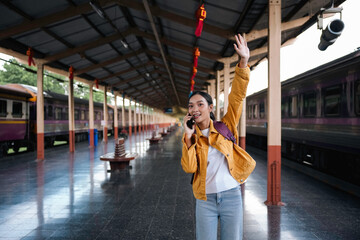 Excited young woman at train station, waving and using phone, ready for journey. Busy platform, smiling faces, bustling atmosphere. Travel photography captures holiday spirit