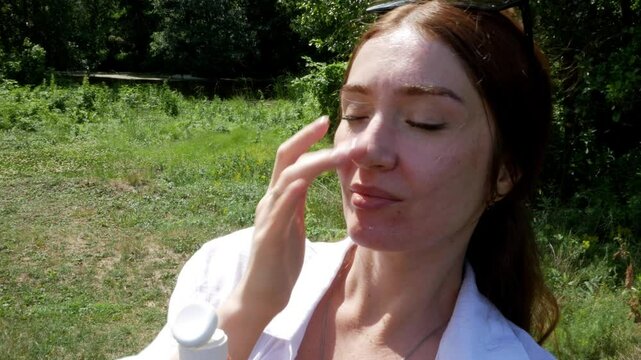 Close-up woman takes sunscreen of tube, moisturizing lotion applies sunblock on her face against the background of nature, in the park, in the forest