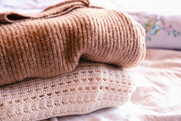 Stack of clean freshly laundered, neatly folded women's clothes on bed. Pile of shirts and sweaters on the bed. Copy space, close up