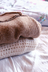 Stack of clean freshly laundered, neatly folded women's clothes on bed. Pile of shirts and sweaters on the bed. Copy space, close up