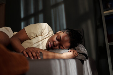Young crying African American woman with post traumatic syndrome lying on bed in home environment...