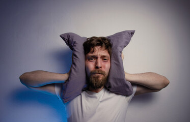 Man having insomnia, can't sleep over the noise that someone is making , putting pillow on the head 