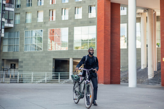 smiling african american businessman in suit with backpack walks with electric bike heading to work