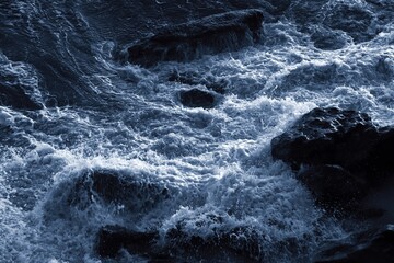 Close-up view of white foam breaking against dark ocean rocks