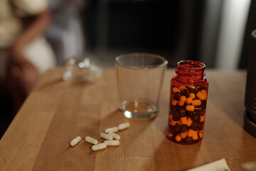 Bottle of pills and pile of antidepressants on wooden table with empty glass for water prepared for person suffering from PTSD