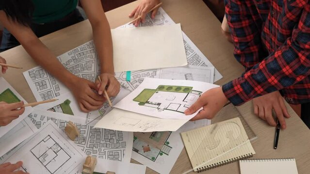 Smart architect and safety engineer discussion about building blueprint on table with architectural document, measurement tools and wooden block scatter around at modern office. Closeup. Delineation.